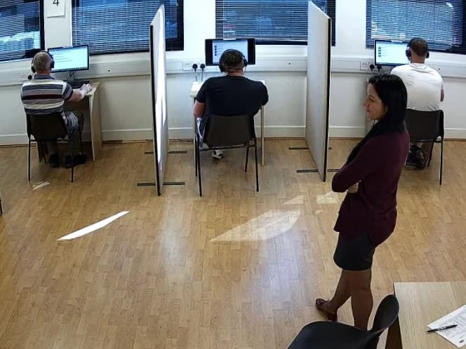 Candidates at screened test desks while an invigilator watches
