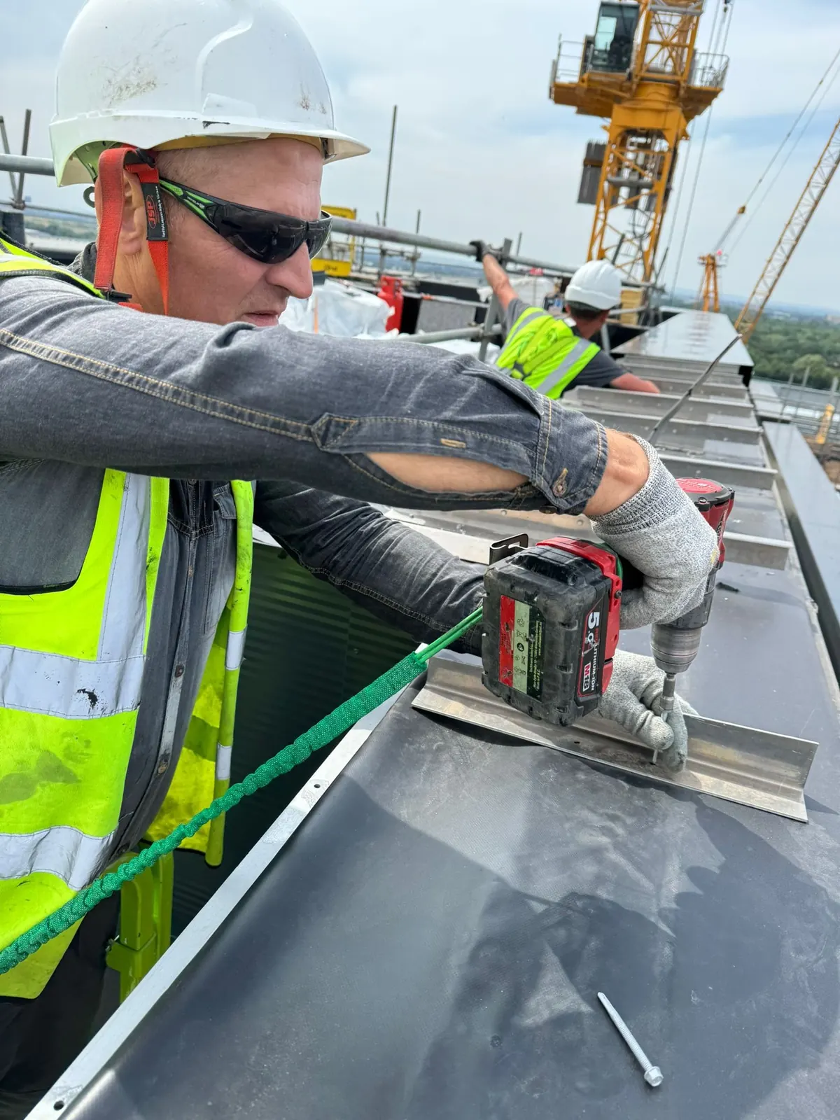 Operative fixing edge trim with a battery drill at height, a tower crane behind